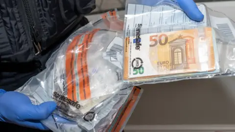 Northamptonshire Police A police officer holding euro cash that has been placed in a bag