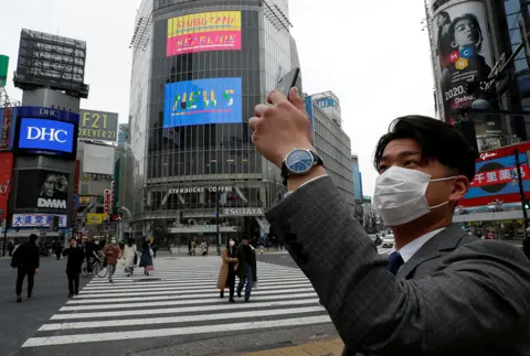 Issei Kato / Reuters A man wearing a protective face mask takes a photo with his mobile phone at noon, at Shibuya Crossing in Tokyo, Japan