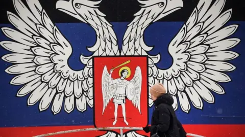 ALEXANDER NEMENOV/AFP A woman walks past the emblem of the DNR in Donetsk