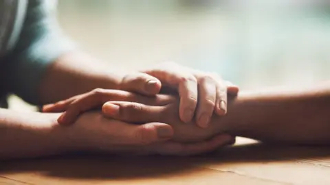 Getty Images One person holding another person's hand to comfort them