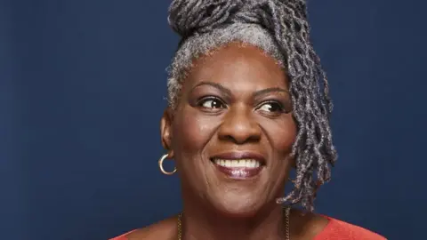 A woman with grey dreadlocks smiles as she looks away from the camera for a portrait photo