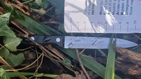 West Midlands Police A kitchen style knife in undergrowth. A measuring guide is next to it, suggesting its blade is about 10.5cm long