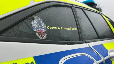 A picture of a logo on the side of a green and blue police car. It reads Devon and Cornwall Police.