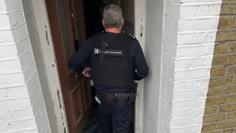 BBC An officer enters a house.