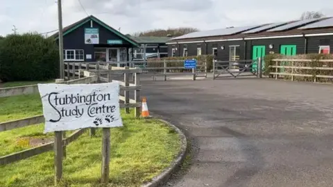 BBC A white sign reading stubbington study centre in front of a brown building with with light brown wooden fencing. 