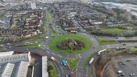 An aerial view of a large estate with a big roundabout in the middle. Cars can be seen driving along the roads.