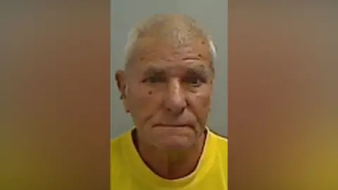 Mugshot of Agar. He is clean shaven with thin white hair, and only appears to have one ear.