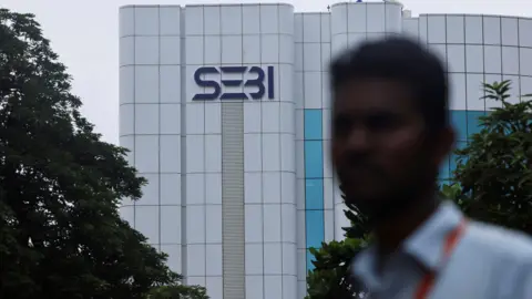 Reuters Seorang pria berdiri di depan logo kantor pusat Dewan Sekuritas dan Bursa India (SEBI) di Mumbai, India, 6 September 2024.