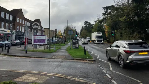 Kingspost parade of shops in Burpham on London Road, cars and other vehicles driving along the road.