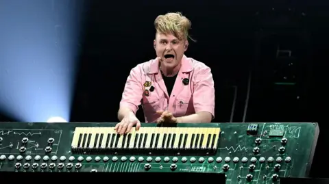 A man stand behind a large keyboard built into what appears to be a large circuit board.