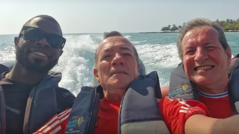L-R Yostin Andres Mosquera, Albert Alfonso and Paul Longworth. They are shown smiling at a camera in a selfie, all wearing life jackets as they sit at the back of a speedboat.