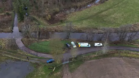 PA Media An aerial view of Abberwick Ford showing a rural road approaching a river with a number of emergency vehicles parked up.