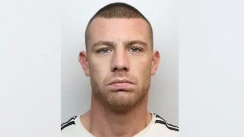 Man in white T-shirt with black stripes on it. He has light stubble.