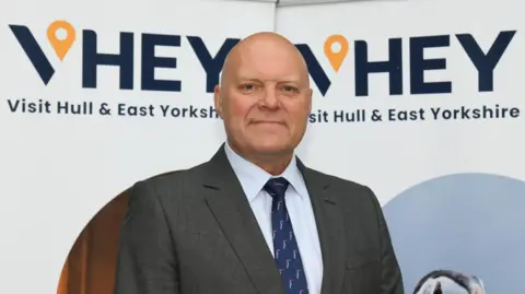 VHEY Portrait of Chris Blacksell, VHEY's chief executive. He is wearing a grey patterned suit, white shirt and dark navy tie