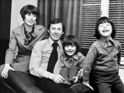 Getty Images A family photo. Cathy Ferguson, Sir Alex and their two sons. The boys and Sir Alex look into the camera smiling, while Cathy looks at her family fondly.