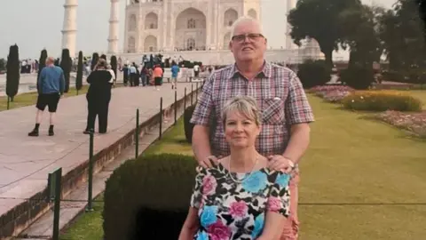 Jan Ball Ian Ball, standing outside the Taj Mahal, in India, with his arm son his wife, Jan Ball, whose sitting down