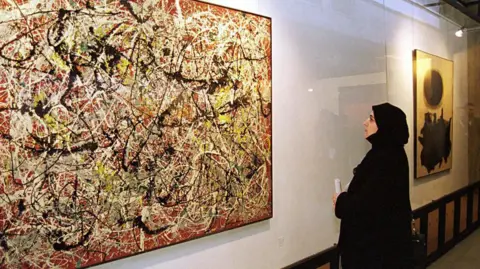 KAVEH KAZEMI/Getty Images Seorang pengunjung wanita memandang lukisan oleh pelukis ekspresionis abstrak Amerika Jackson Pollock di Museum Seni Kontemporer Teheran pada tahun 1999