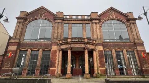 Burslem School of Art, a building with large windows - including two large arched windows on its second floor - and a central entrance way surrounded by four brick pillars.