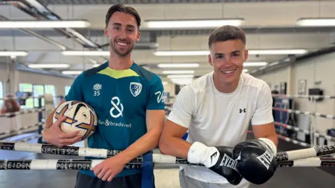 Owen and Taylor Bevan pose for a photo while standing inside a boxing ring