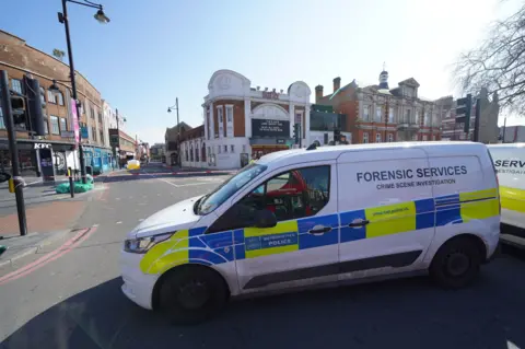 PA Media A forensic services van in front of a white and yellow police tent and cordon on Brixton Road 