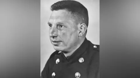 A black and white head and shoulders photograph of a Sheffield firefighter wearing a traditional uniform