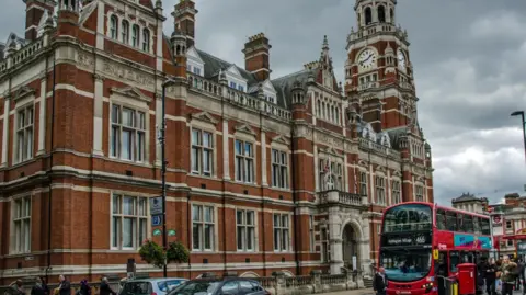 Croydon town hall, a red brick building with flags outside and a red bus at a stop.