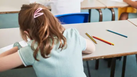 Schoolgirl writing at classroom desk in primary school lesson.