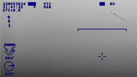 NPAS Infra-red camera image taken from a helicopter. There is an arrow pointing to an indistinct object. There are blue letters and numbers plus other types of on-screen information.