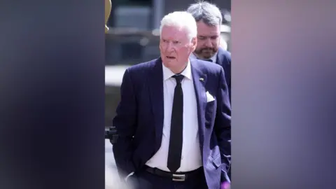 PA Media A man with white hair wears a navy suit and black tie