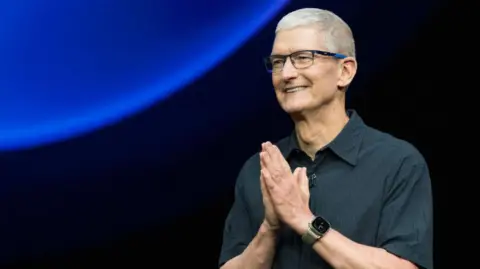 Getty Images Apple CEO Tim Cook holds his hands together in a prayer pose while speaking during Apple's "It's Glowtime" event in Cupertino, California, September 9, 2024. 