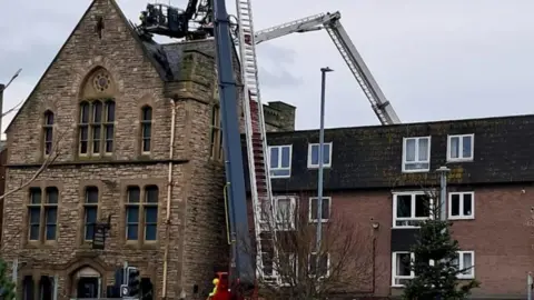 DWFRS Firefighters on a aerial ladder going up to the roof of a three-storey building 