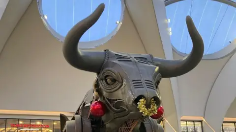 A photo of a bull with tinsil around it's nose as a nosering. He also has red baubles hanging from his ears. 