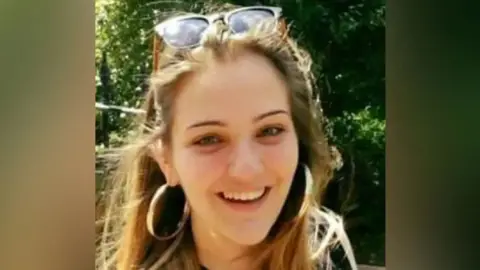 Handout Ms Espirito Santo has blond hair and is smiling with gold hoop earrings and glasses on her head. 