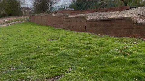 View of the grass embankment with a brick wall behind it with large cracks