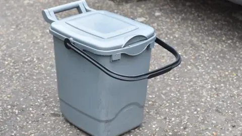 PCC A food caddy; a grey plastic bin with handle and lid. 