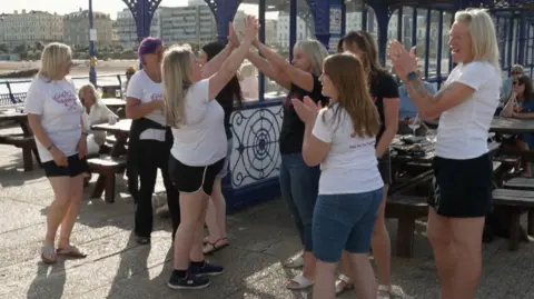 A group of eight women in black and white shirts dancing on a pier.