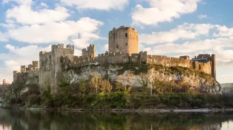 University of Aberdeen Pembroke Castle, on the banks of a river and surrounded by trees. It has tall and uneven stone walls