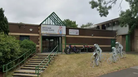 Google Steps leading up to brick leisure centre with metal sculptures of a family on bikes to the right of the image