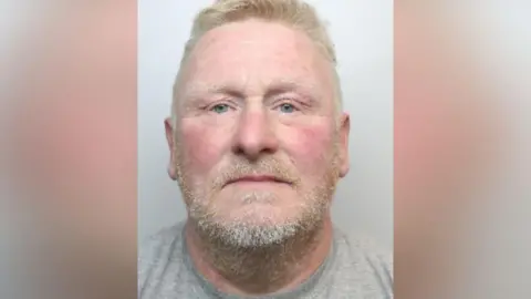 West Yorkshire Police A mugshot of Claughton, who is wearing a light grey T‑shirt. He has short, light‑coloured hair and a neatly trimmed beard. The background is plain and light.