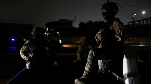 Reuters Two people in military fatigues sit in the bed of a truck in a street enveloped in darkness