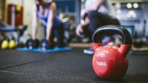 A kettlebell in the foreground of a shot of peoplee exercising in a gym