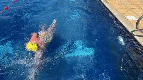 The lane occupies most of the image, with one swimmer in the foreground. Two other people swimming are nearer to the other end of the pool.