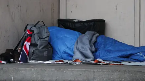 PA Media Homeless person in a blue sleeping bag sleaeping in a doorway.