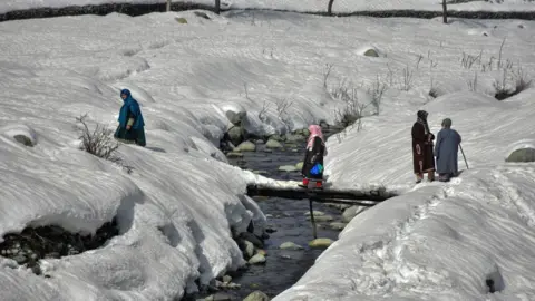 Getty Images TANGMARG, KASHMIR, INDIA - 2023/02/15: Residents cross the snow covered foot-bridge during a sunny winter day in Tangmarg, about 50kms from Srinagar, the summer capital of Jammu and Kashmir.