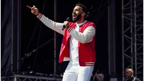 Tom Langford Craig David performing onstage wearing white trousers and a red jacket at Victorious Festival