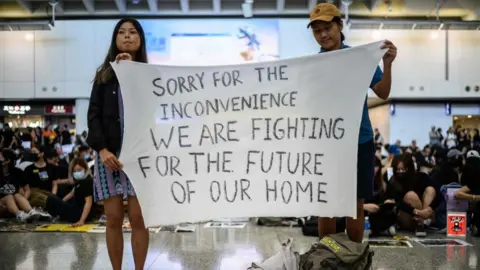 AFP/Getty Hong Kong activists at an airport rally hold a banner reading: "Sorry for the inconvenience we are fighting for the future of our home", 9 August 2019