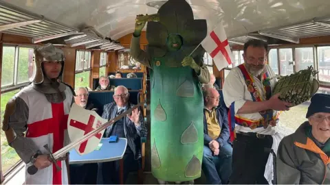A man dressed as an asparagus, with a man dressed as St George shown on board a steam train