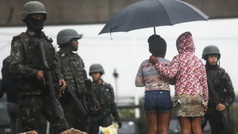 Getty Images Youngsters stand near Brazilian soldiers during a "Mega Operation" conducted by the Brazilian Armed Forces along with police against gang members in seven of Rio's most violent "favela" communities on August 21, 2017 in Rio de Janeiro, Brazil.