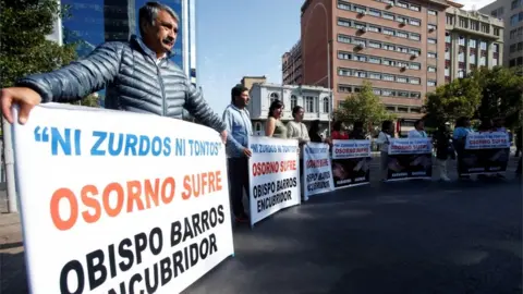 Reuters People hold banners reading "Neither lefties nor fools, Osorno suffers, Bishop Barros, accessory after the fact," during visit