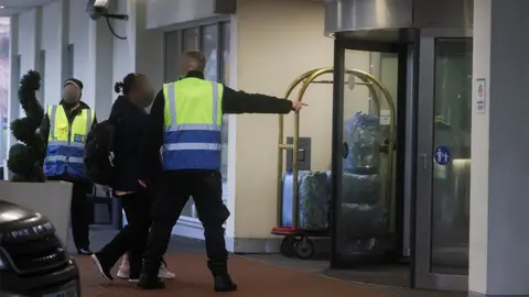 Reuters A woman is given instructions by a G4S guard as she arrives at a Heathrow quarantine hotel in February